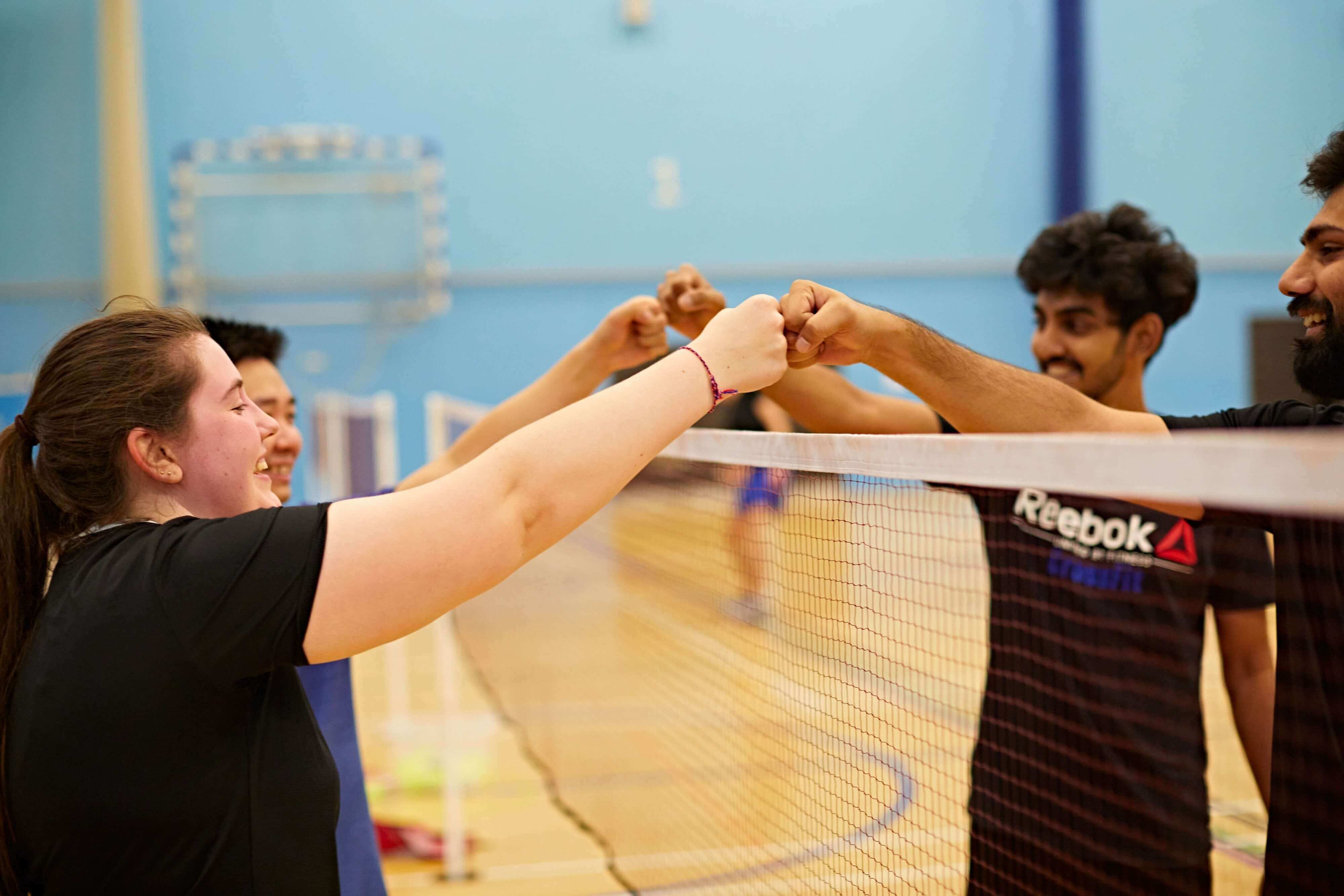 Four students fist bumping at the end of a badminton match